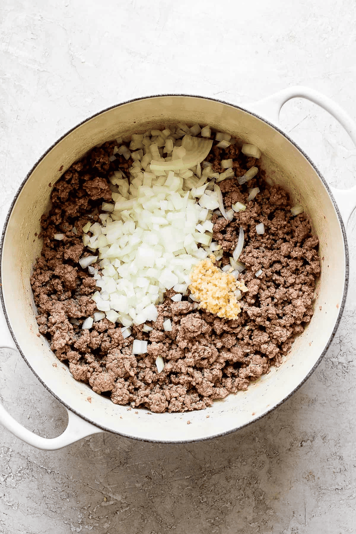 Browned ground beef, diced onion, and minced garlic in a white dutch oven.