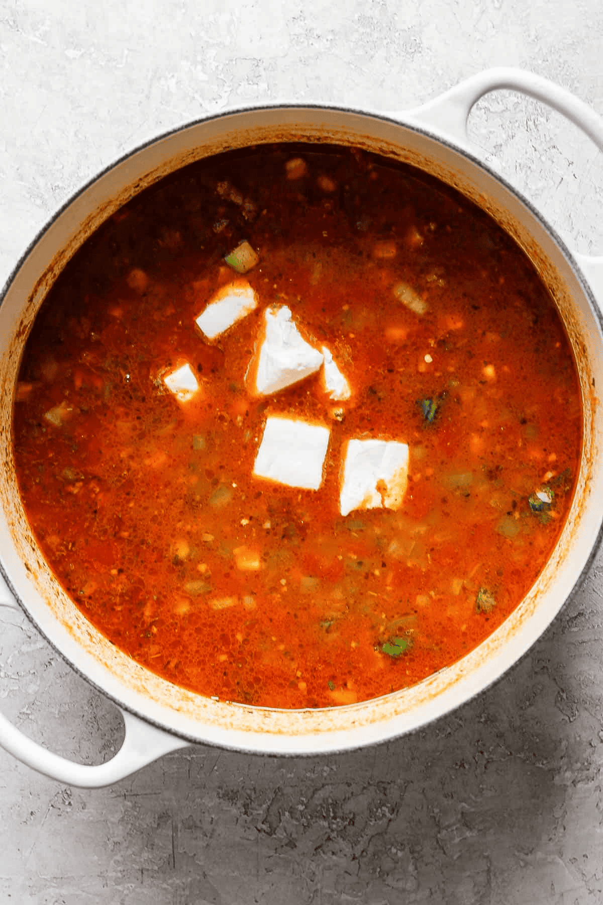 Chunks of cream cheese added to a pot of taco soup.