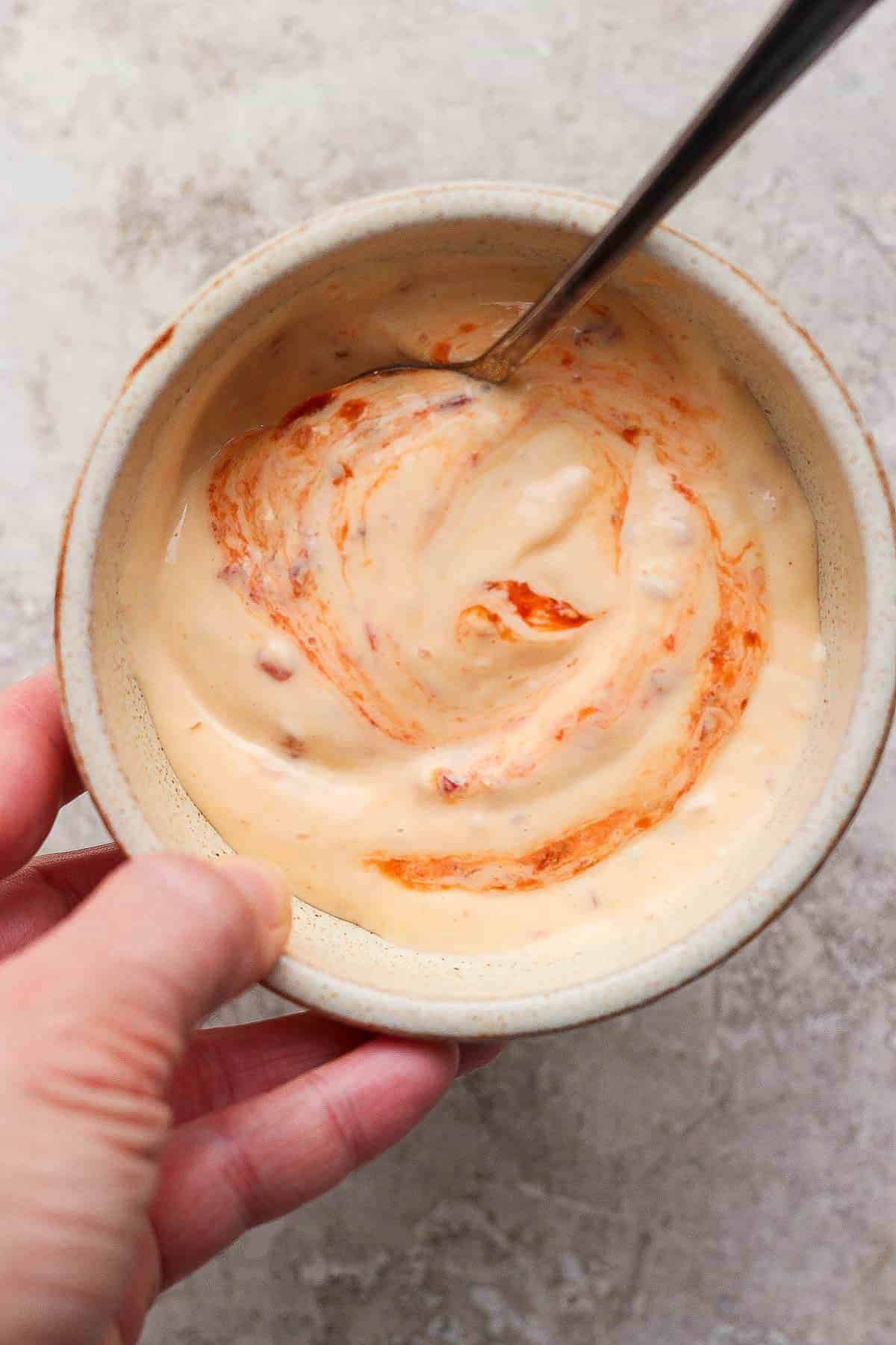 Chili garlic mayo in a small bowl with a spoon sticking out the side and being held by a hand.