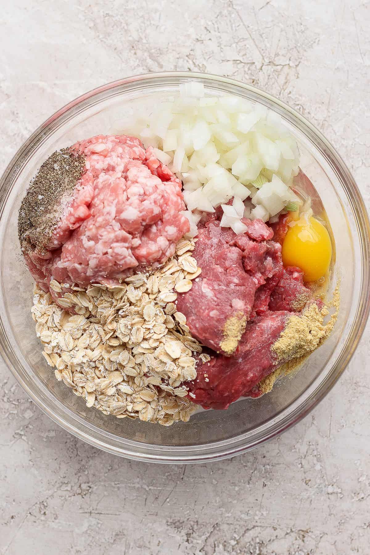 Ingredients for a healthy meatloaf in a glass bowl before being mixed together.