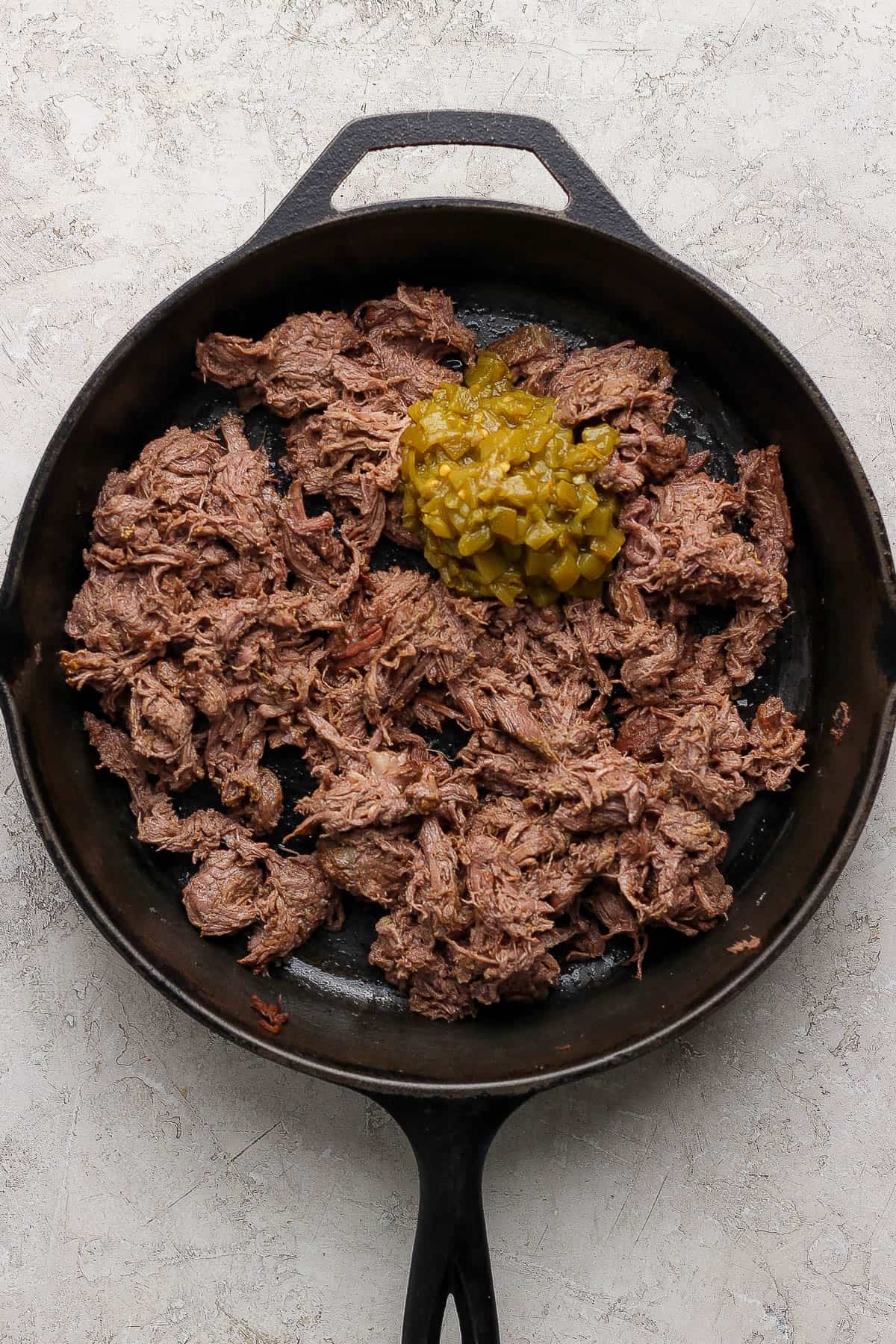 Cooked, shredded beef in a skillet with canned green chiles before being added to sheet pan enchiladas.