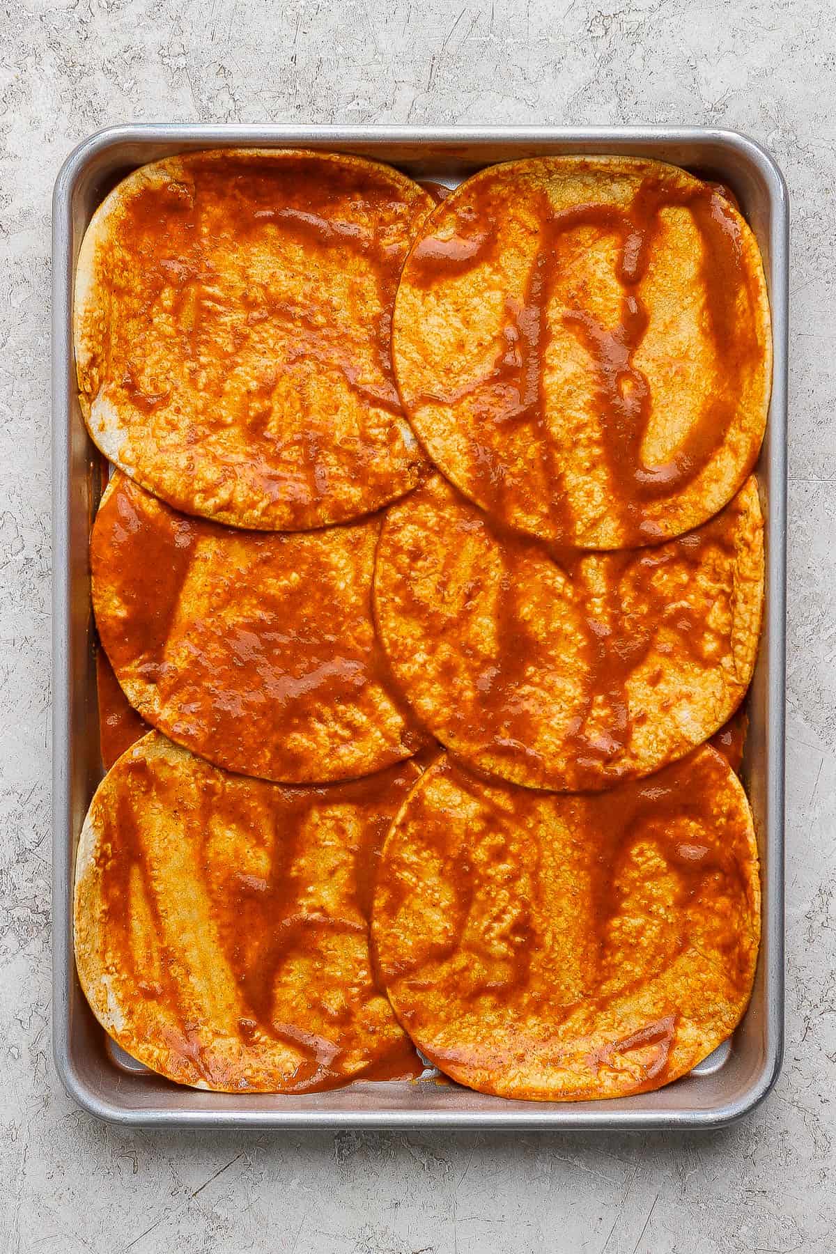 The bottom tortilla and enchilada sauce layer of sheet pan enchiladas in a quarter sheet pan.