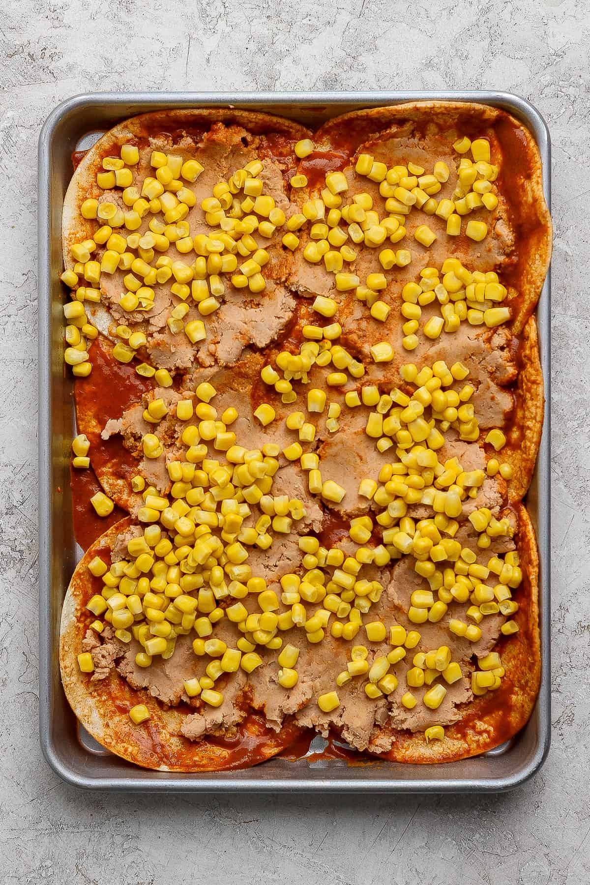 Refried beans and canned corn added to the bottom layer of sheet pan enchiladas.
