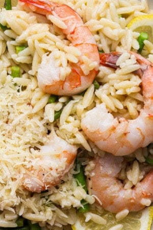 A plate of shrimp scampi orzo with asparagus, fresh lemon and shredded parmesan.
