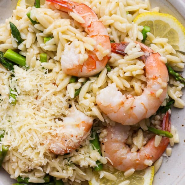 A plate of shrimp scampi orzo with asparagus, fresh lemon and shredded parmesan.