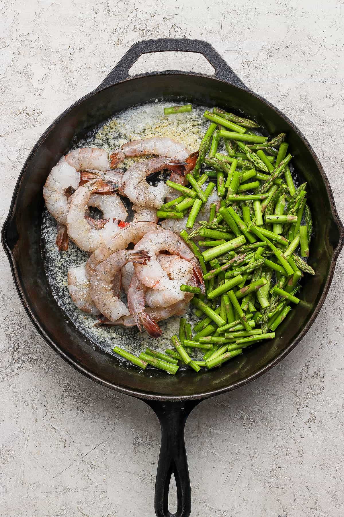 Raw shrimp and asparagus added to a cast iron with sautéed garlic.