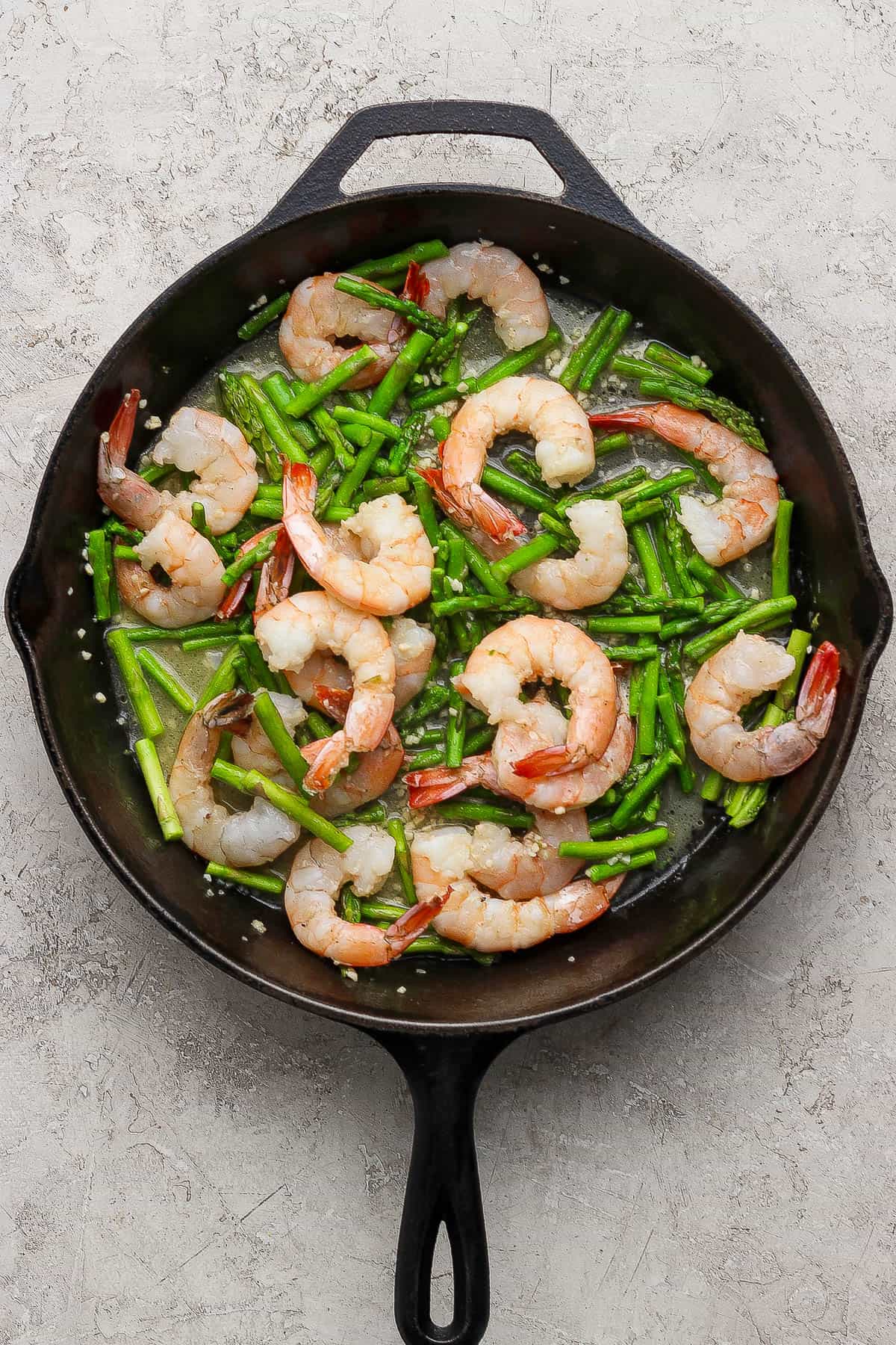 Cooked shrimp scampi and asparagus in a cast iron skillet.