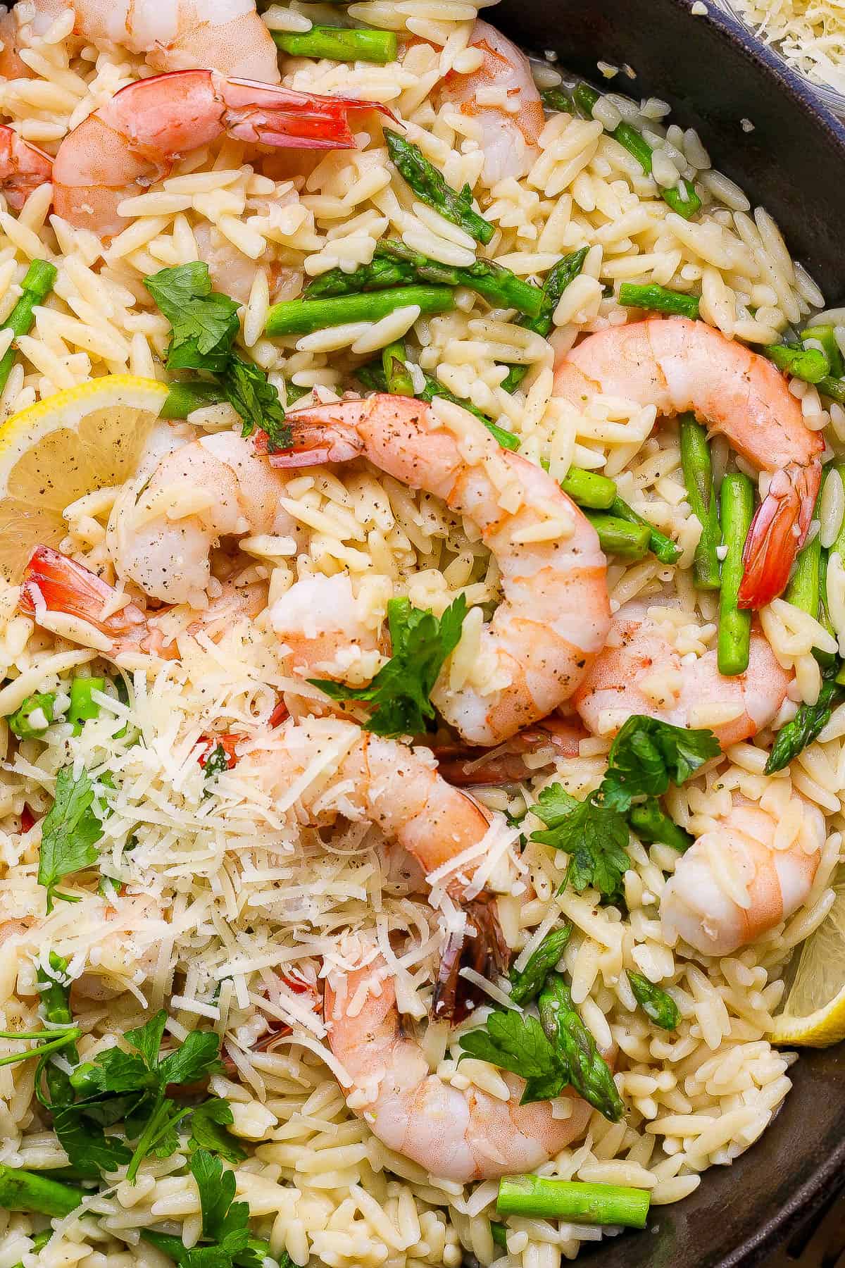 Freshly grated parmesan added to a skillet of shrimp scampi with orzo.