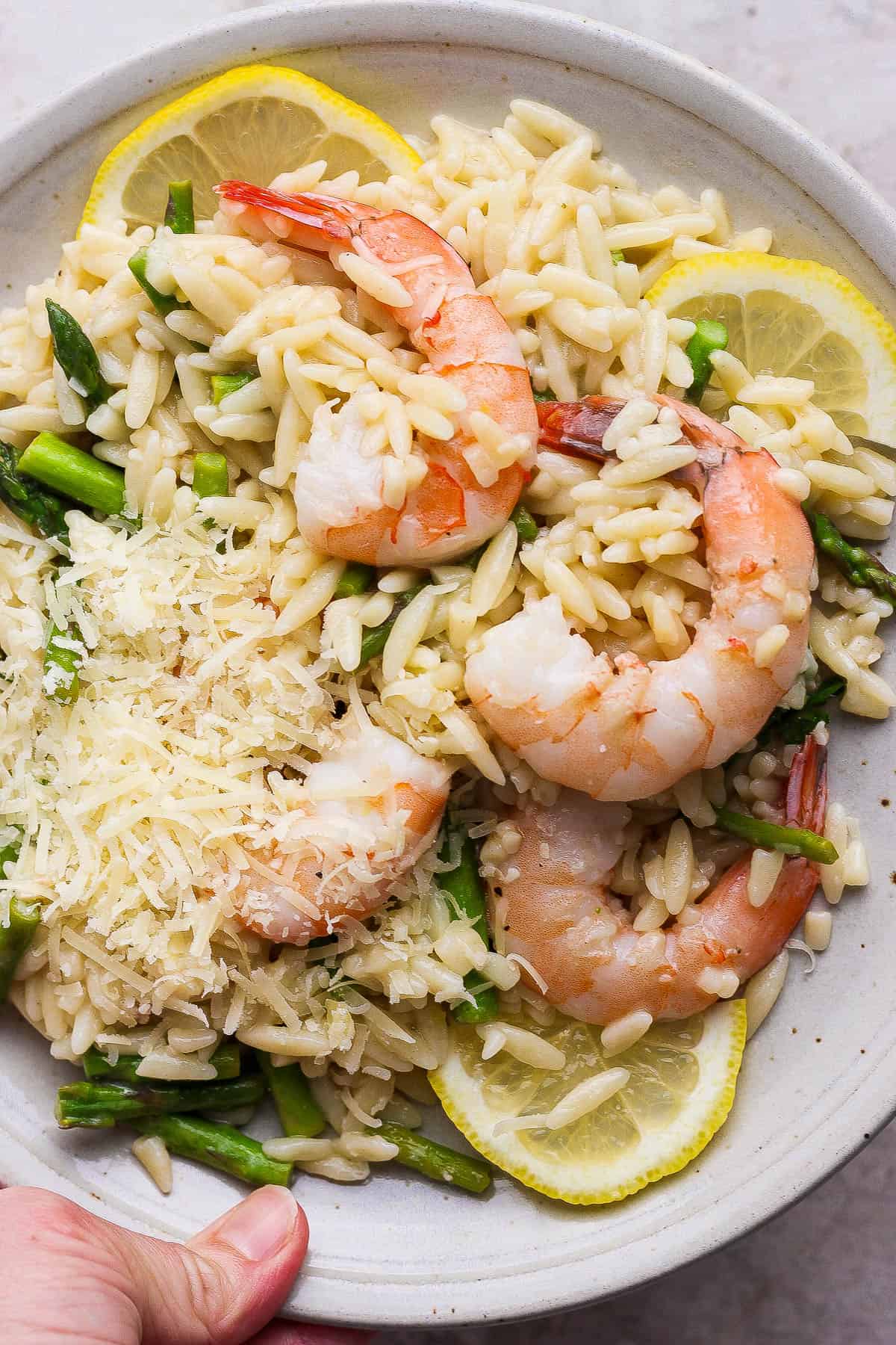 Shrimp scampi with orzo on a plate with parmesan cheese and lemon slices.