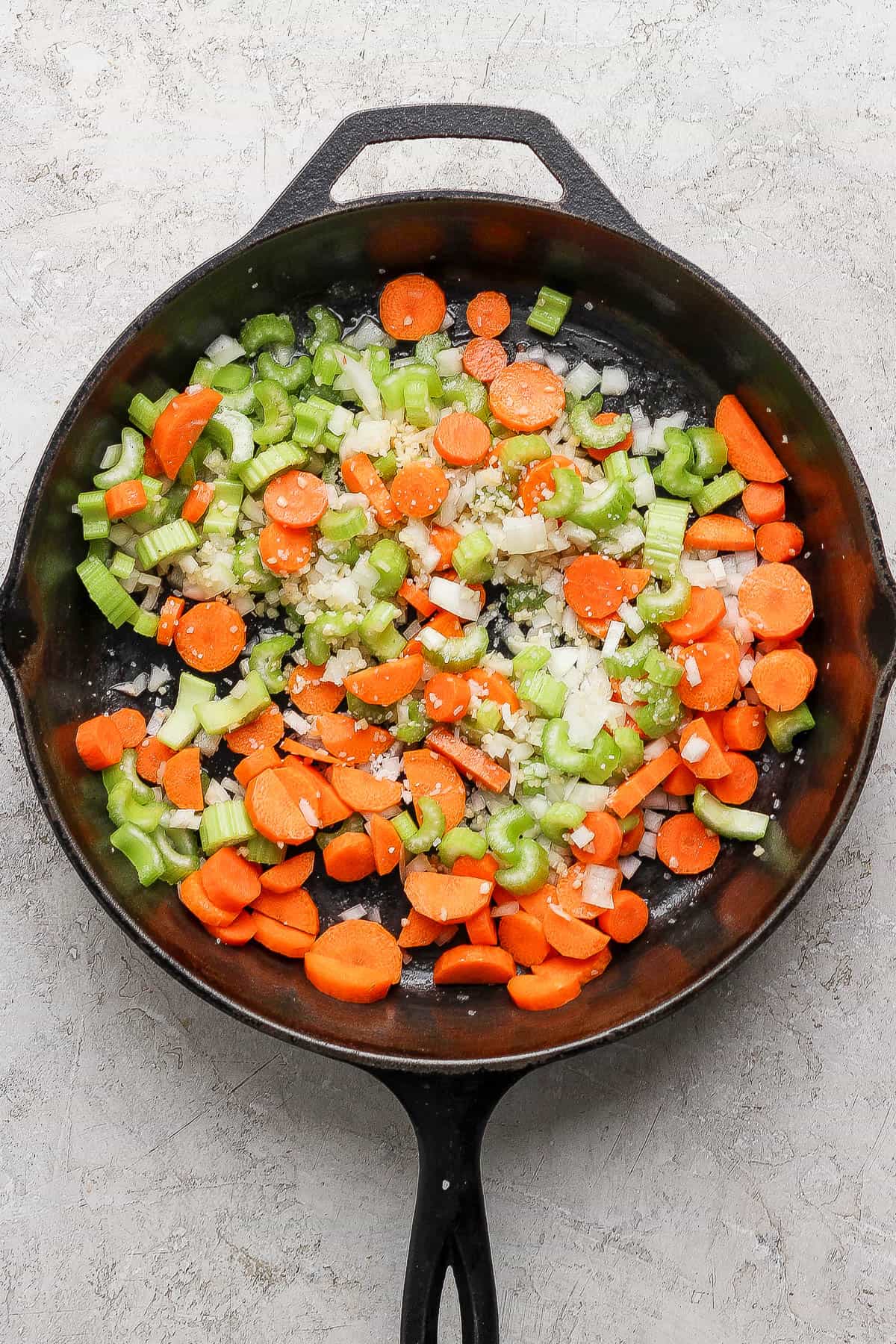Cast iron skillet with carrot, onions and celery cooking inside.