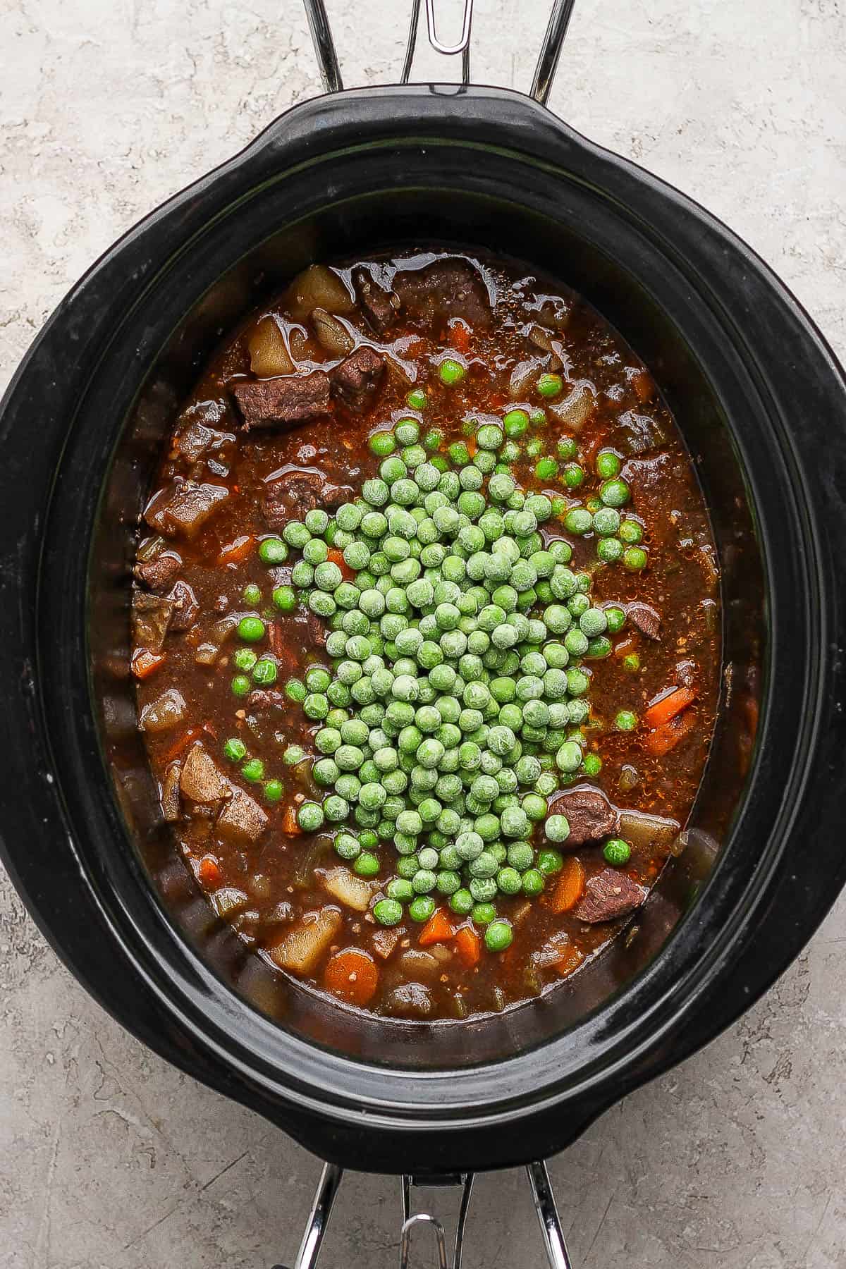 A crockpot full of venison stew with peas on top. 
