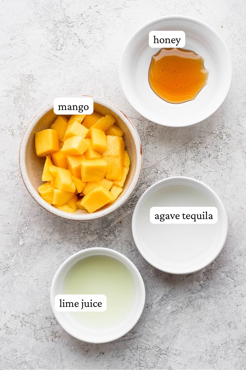 Frozen mango margarita recipe ingredients in individual bowls; honey, mango, agave tequila, and lime juice.