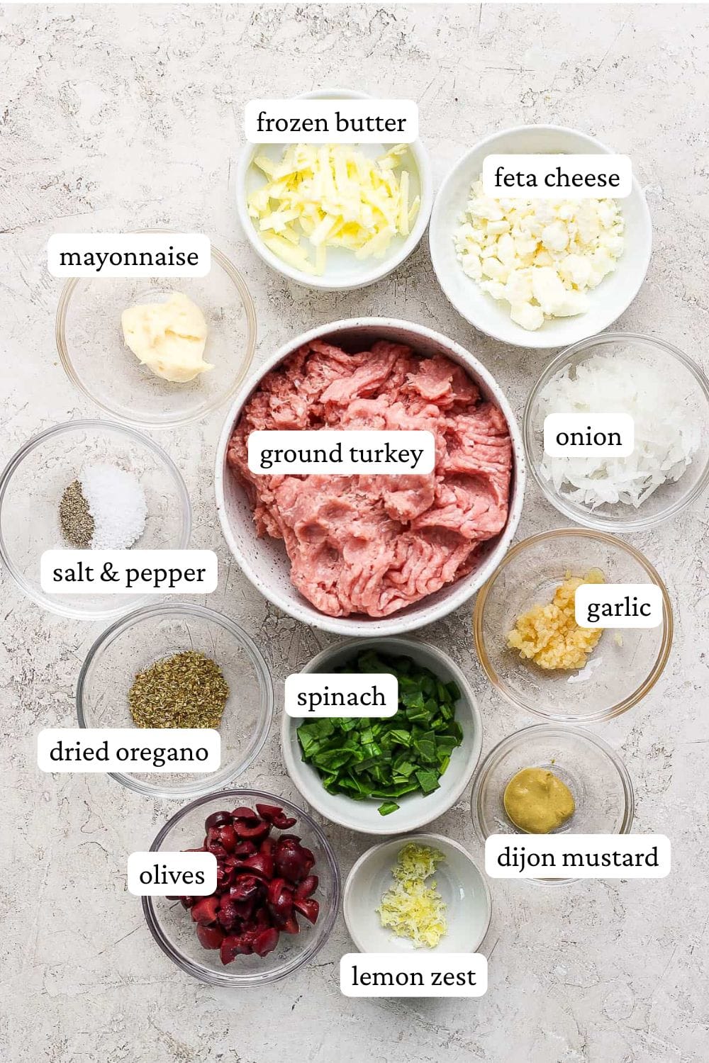 Greek turkey burgers with tzatziki sauce ingredients including frozen butter, feta cheese, mayo, ground turkey, onion, salt and pepper, garlic, dried oregano, spinach, dijon mustard, olives, and lemon zest.