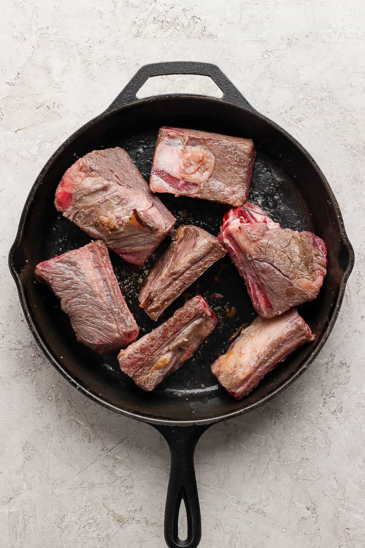 Seven beef short ribs being seared in a cast iron skillet to make beef short rib soup.