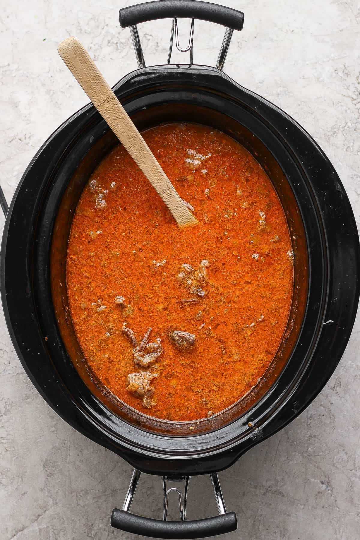 Every soup ingredient in a slow cooker except for vegetables and noodles to make beef short rib soup.