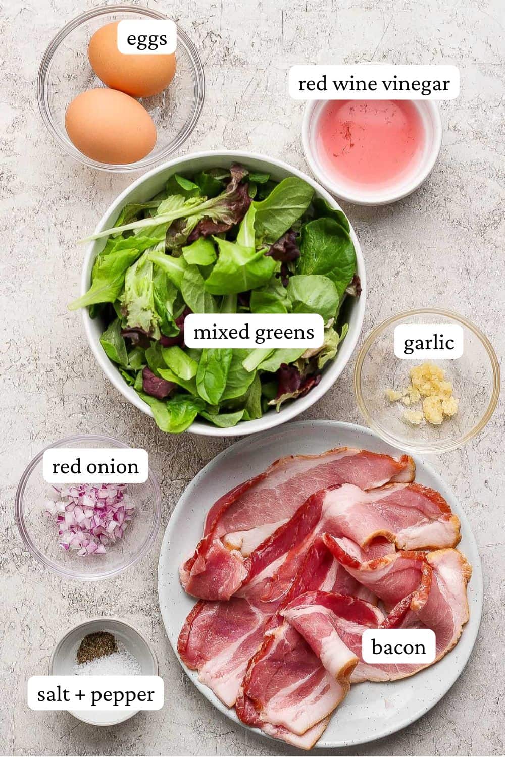 Breakfast salad ingredients in individual bowls such as eggs, red wine vinegar, mixed greens, garlic, red onion, bacon, and salt and pepper.