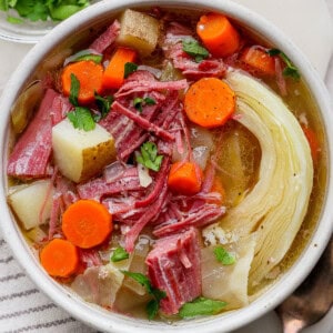 A bowl of corned beef and cabbage soup next to a kitchen towel and gold spoon.