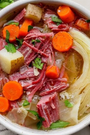 A bowl of corned beef and cabbage soup next to a kitchen towel and gold spoon.