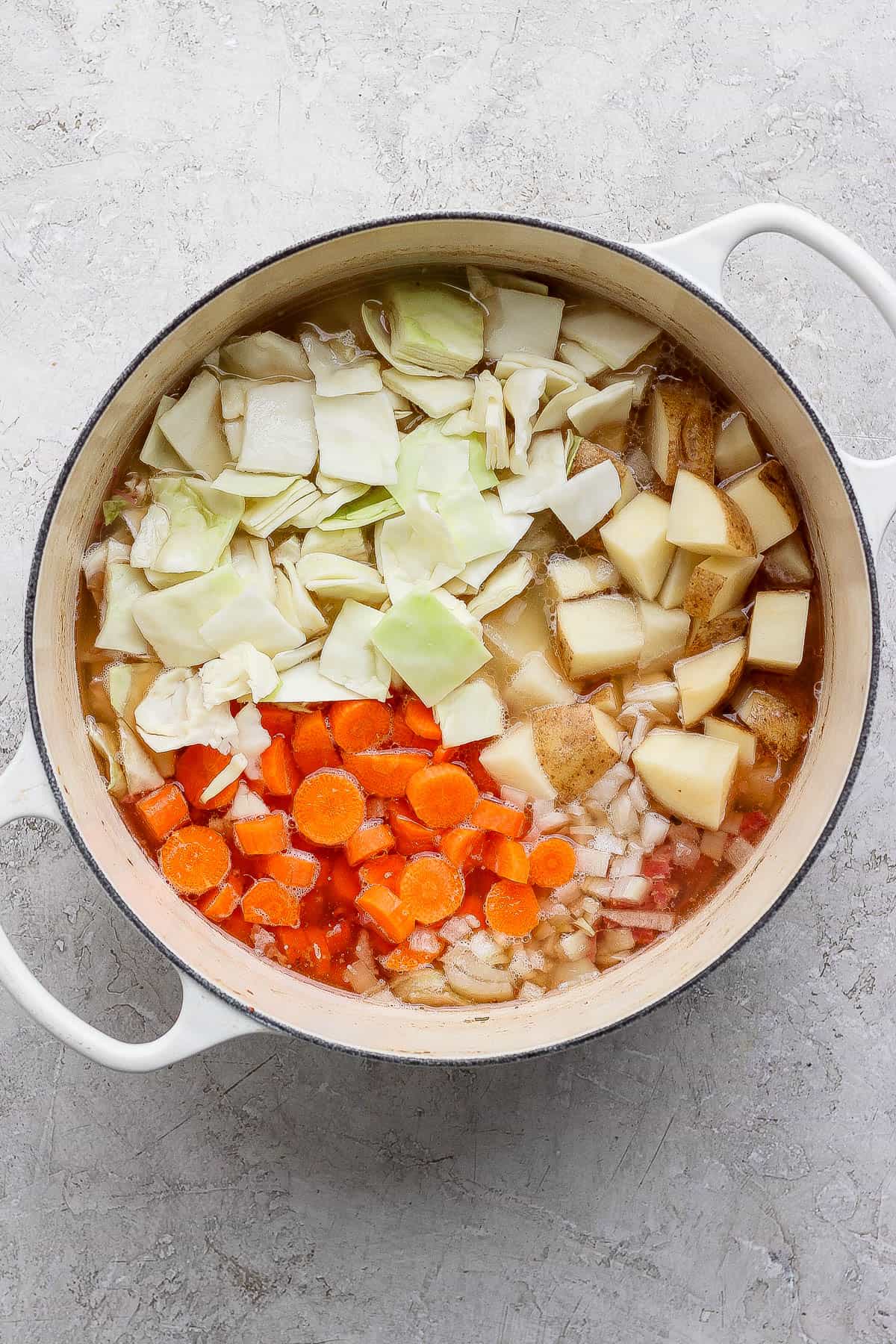 Corned beef and cabbage soup with the onion and vegetables added to the pot but not cooked.