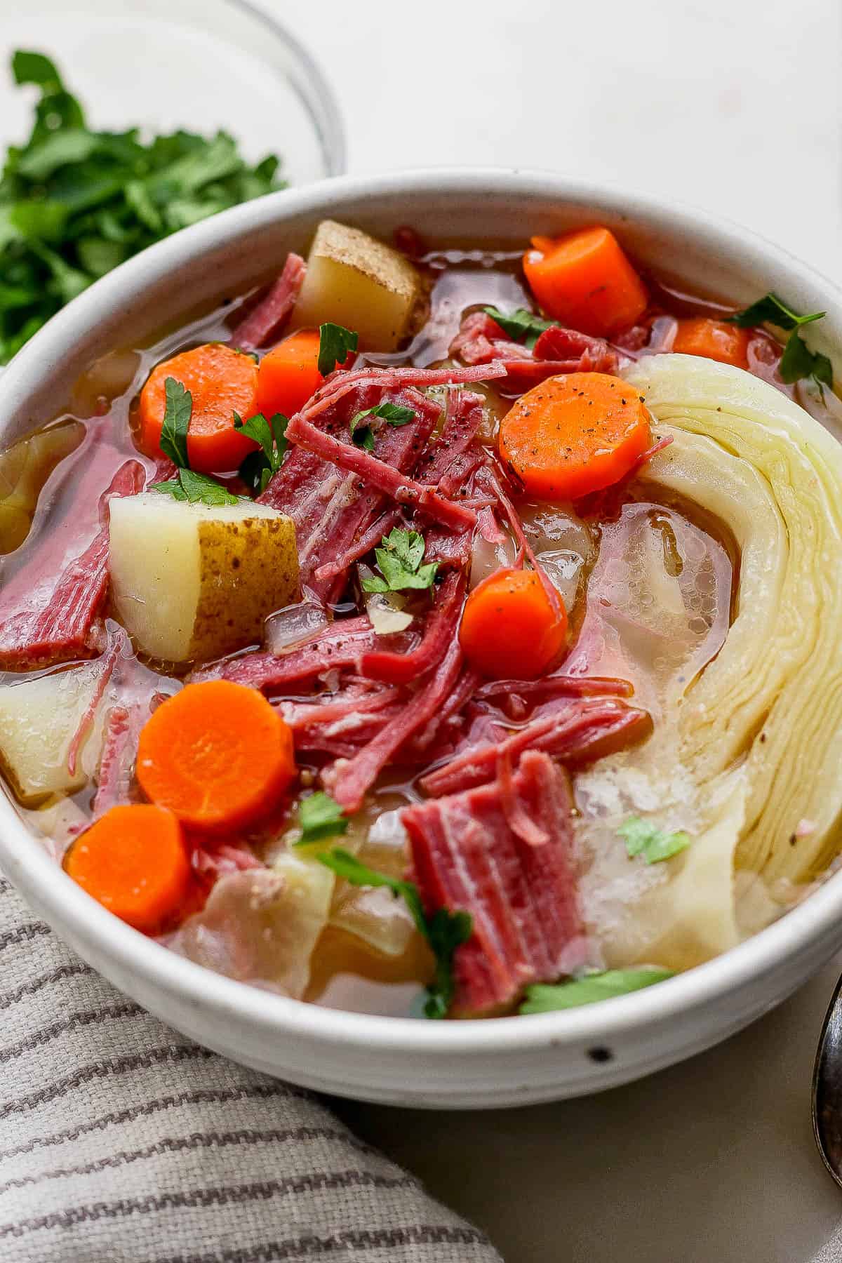 A bowl of corned beef and cabbage soup next to a kitchen towel.