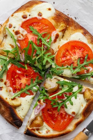 A roasted garlic pizza cut into four pieces on parchment paper.