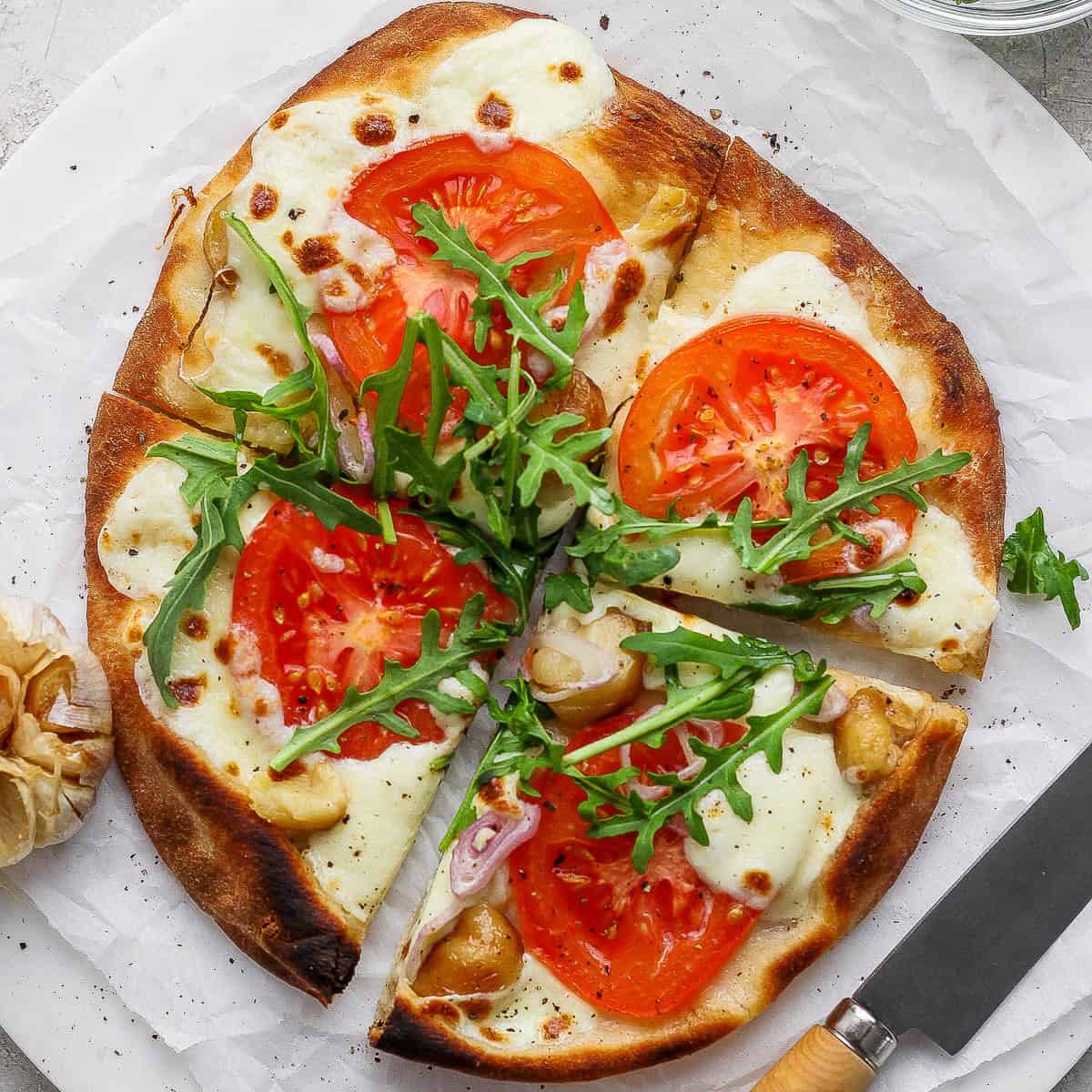 A roasted garlic pizza cut into four pieces on parchment paper.