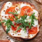 A roasted garlic pizza with arugula on top sitting on a parchment lined baking sheet.