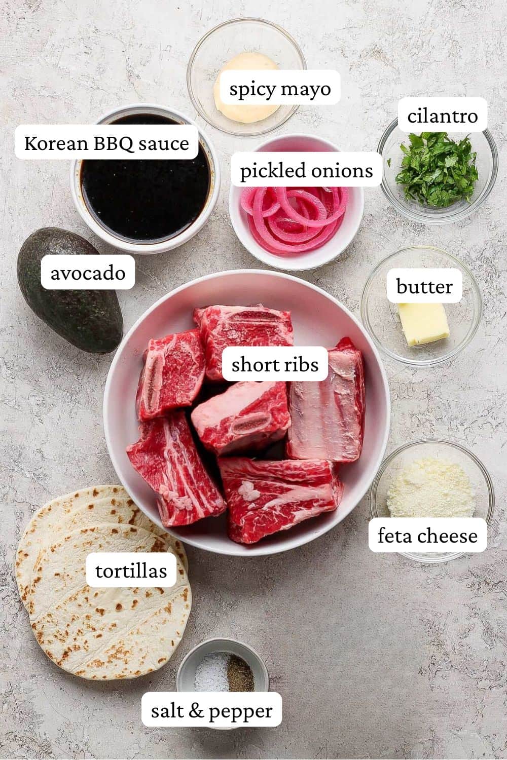 Short rib taco ingredients in individual bowls; spicy mayo, korean bbq sauce, pickled onions, cilantro, butter, avocado, short ribs, feta cheese, tortillas, and salt and pepper