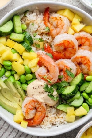 A fully assembled shrimp sushi bowl next to small bowls of fresh ingredients.