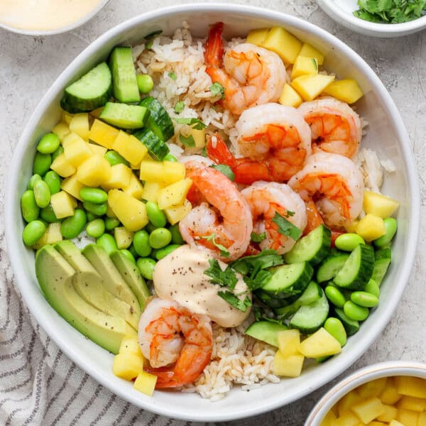 A fully assembled shrimp sushi bowl next to small bowls of fresh ingredients.