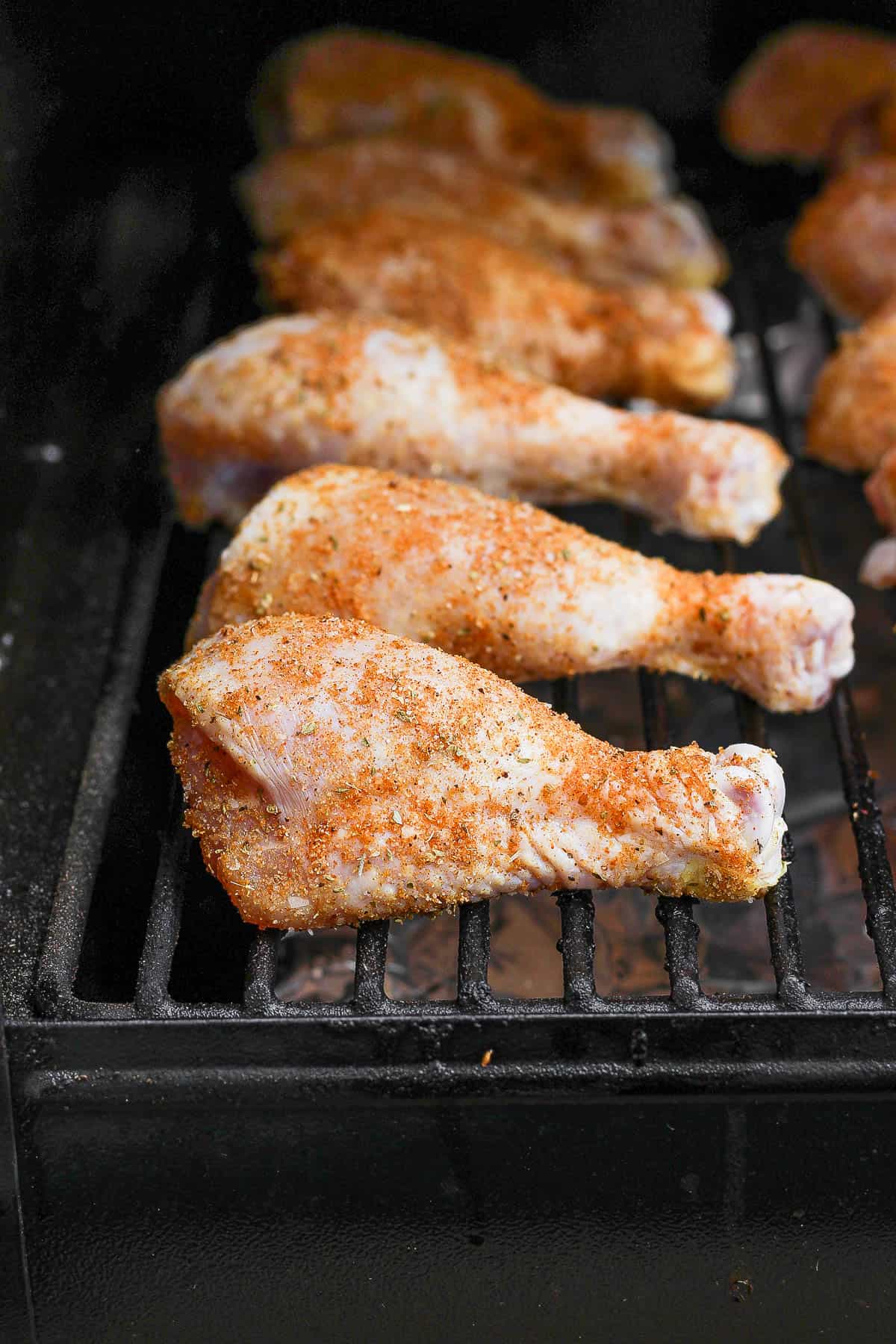 Seasoned chicken legs on the grates of a smoker.