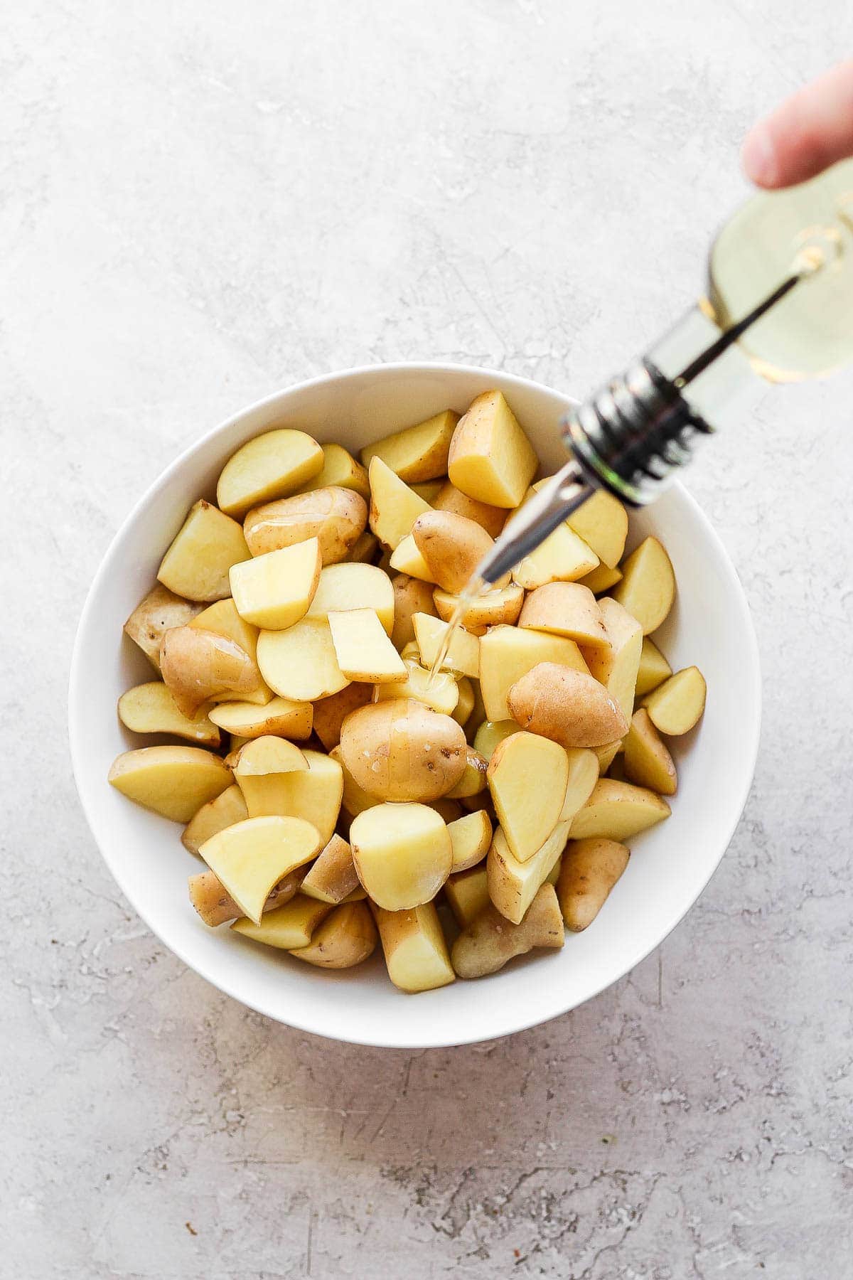 Oil being drizzled on cubed potatoes before being seasoned for the smoker.