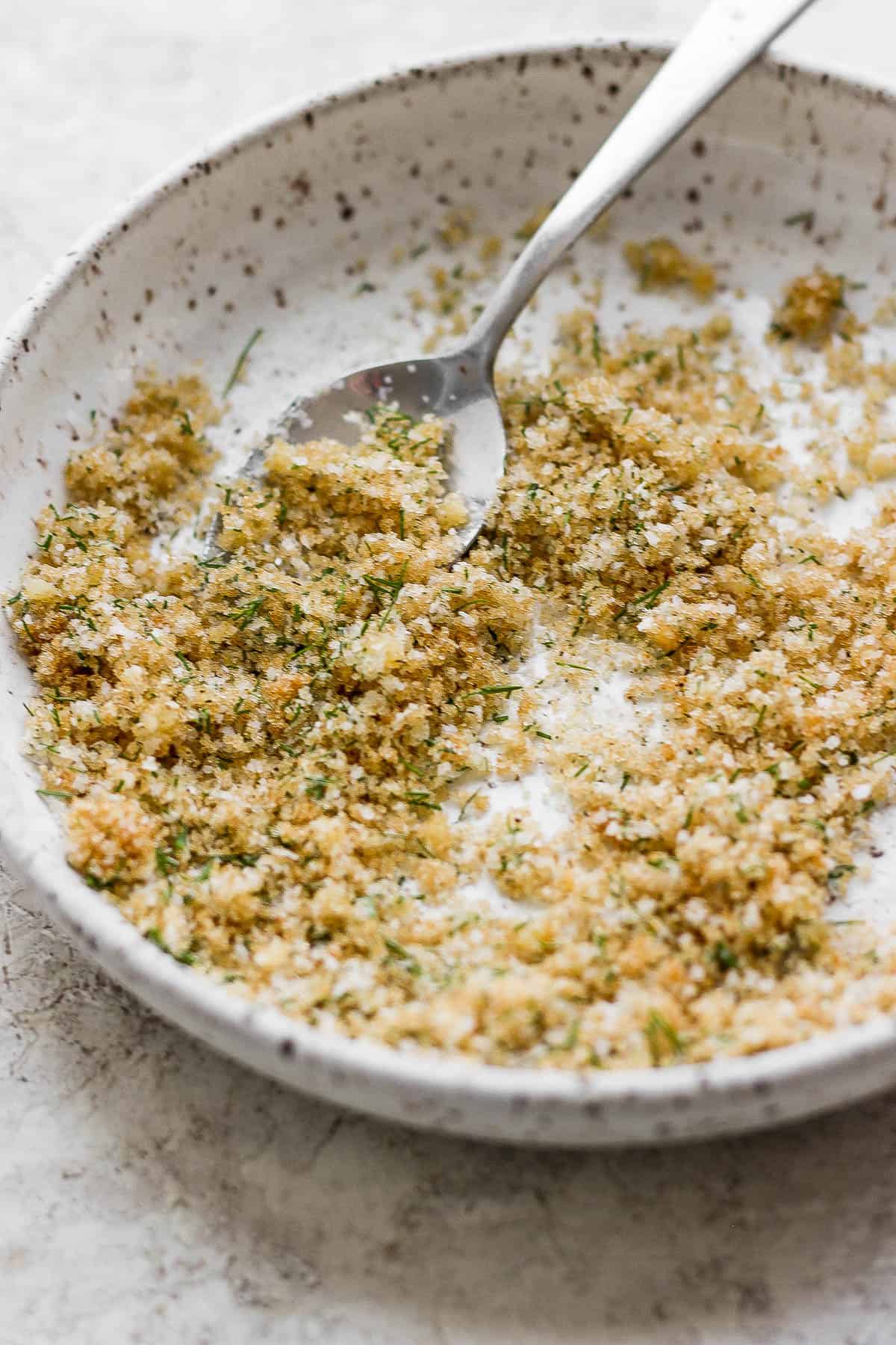 A fully mixed dry brine for smoked salmon in a shallow bowl with a spoon.