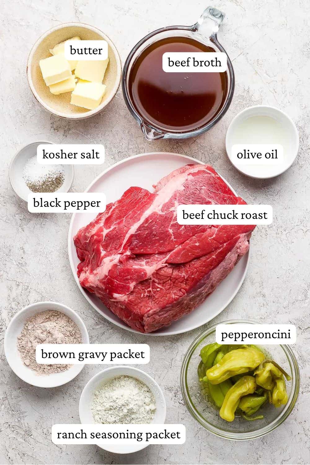 Dutch oven Mississippi Pot roast ingredients including butter beef broth, kosher salt, black pepper, olive oil, beef chuck roast, gravy packet, ranch seasoning packet, and pepperoncini.