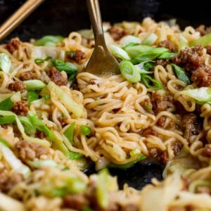 A fork twirling cabbage and noodles in the cast iron skillet.