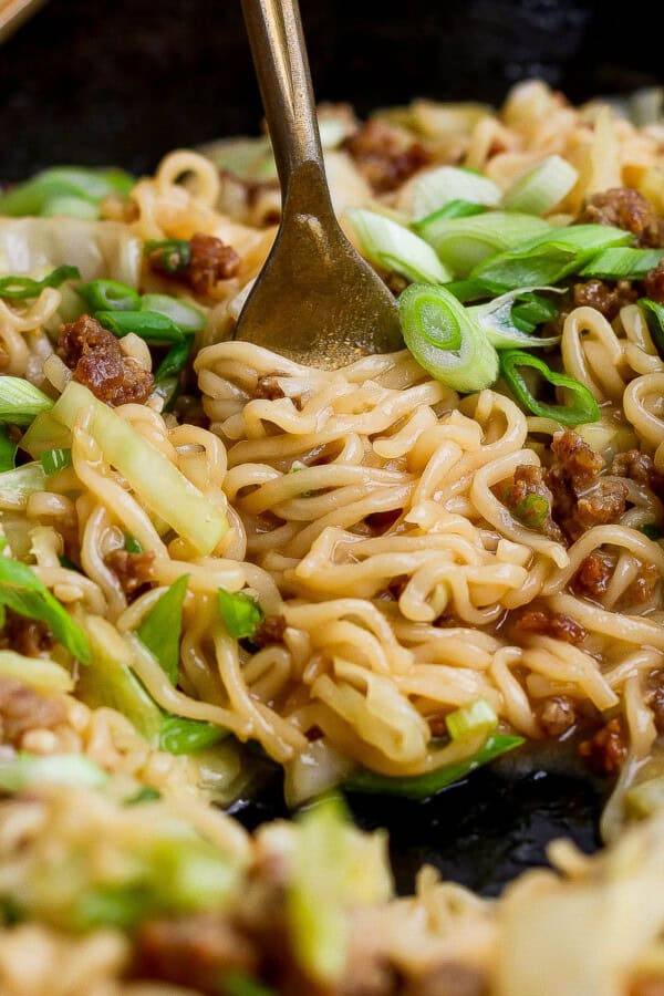 A fork twirling cabbage and noodles in the cast iron skillet.