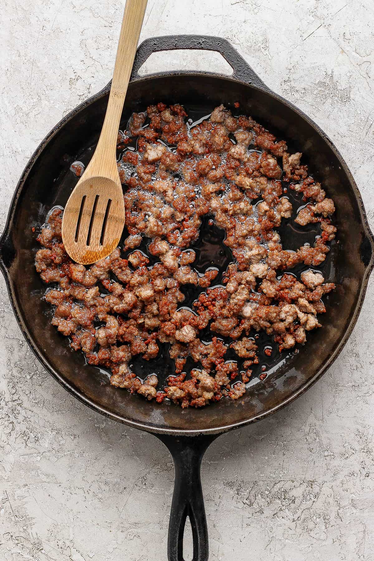 Ground pork browning in a cast iron skillet with a wooden spoon.