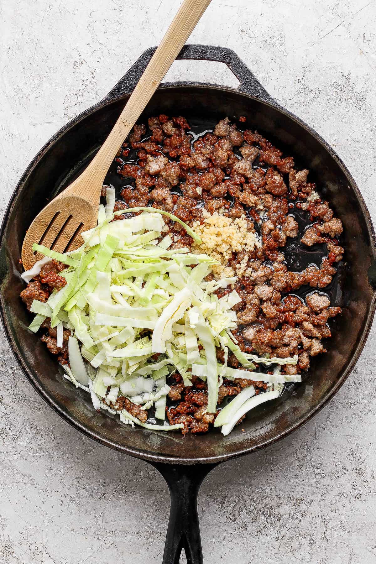 Cabbage and garlic added to a skillet of crispy pork for cabbage and noodles.
