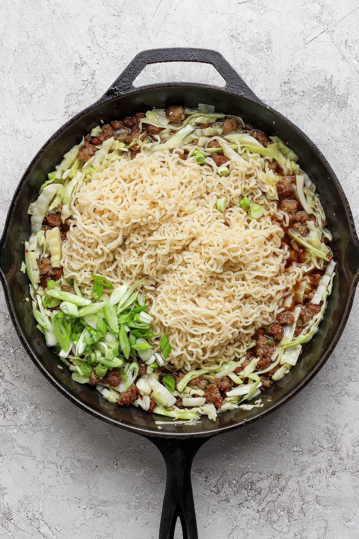 Cabbage and noodles in a cast iron skillet before it is all tossed together.