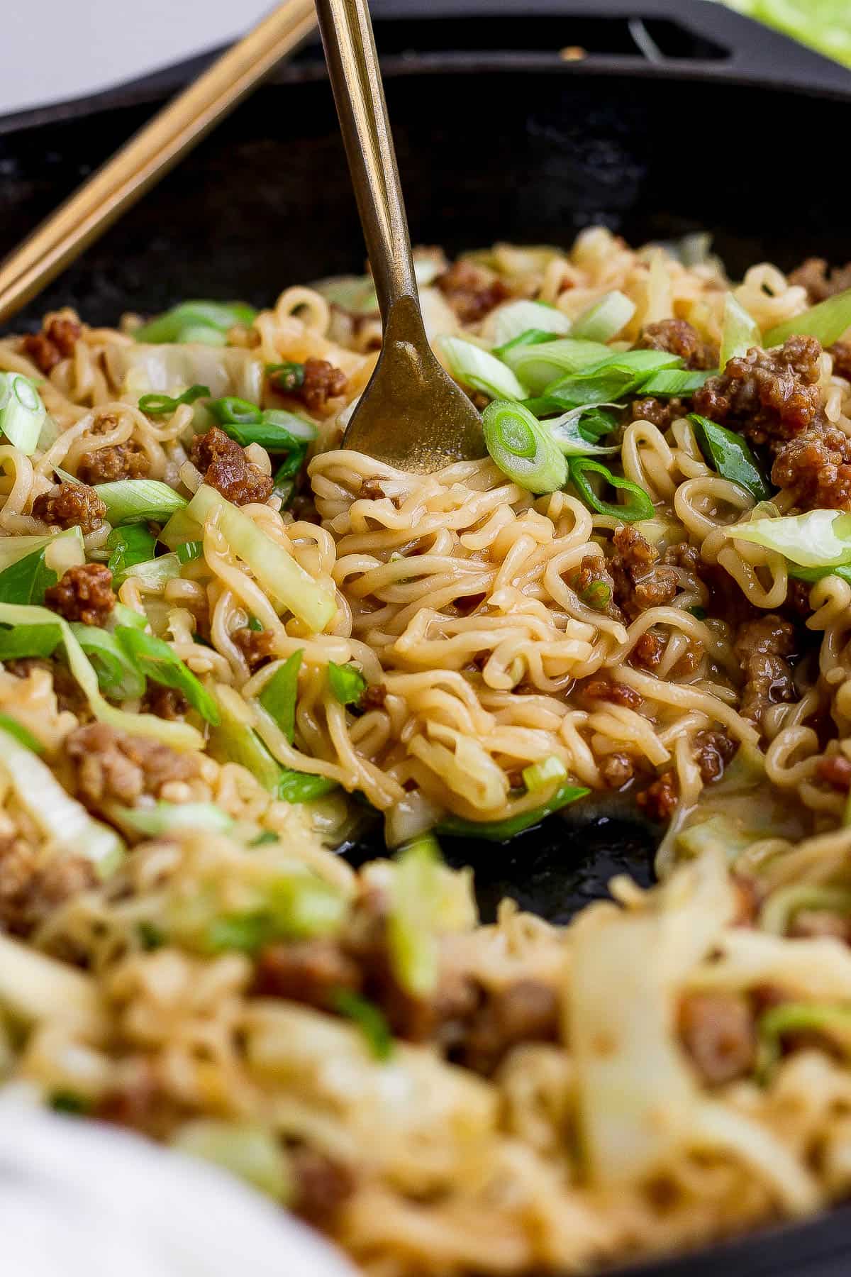 A fork twirling cabbage and noodles in a cast iron skillet.