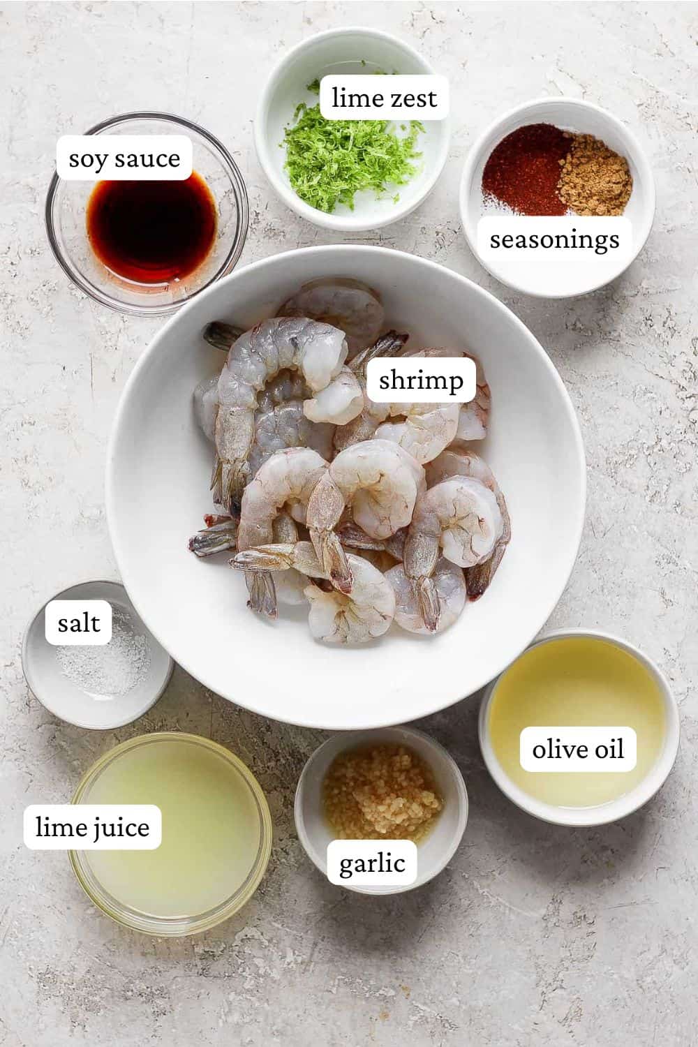 Chili lim shrimp ingredients in individual bowls including raw shrimp, soy sauce, lime zest, seasonings, salt, lime juice, garlic, and olive oil.