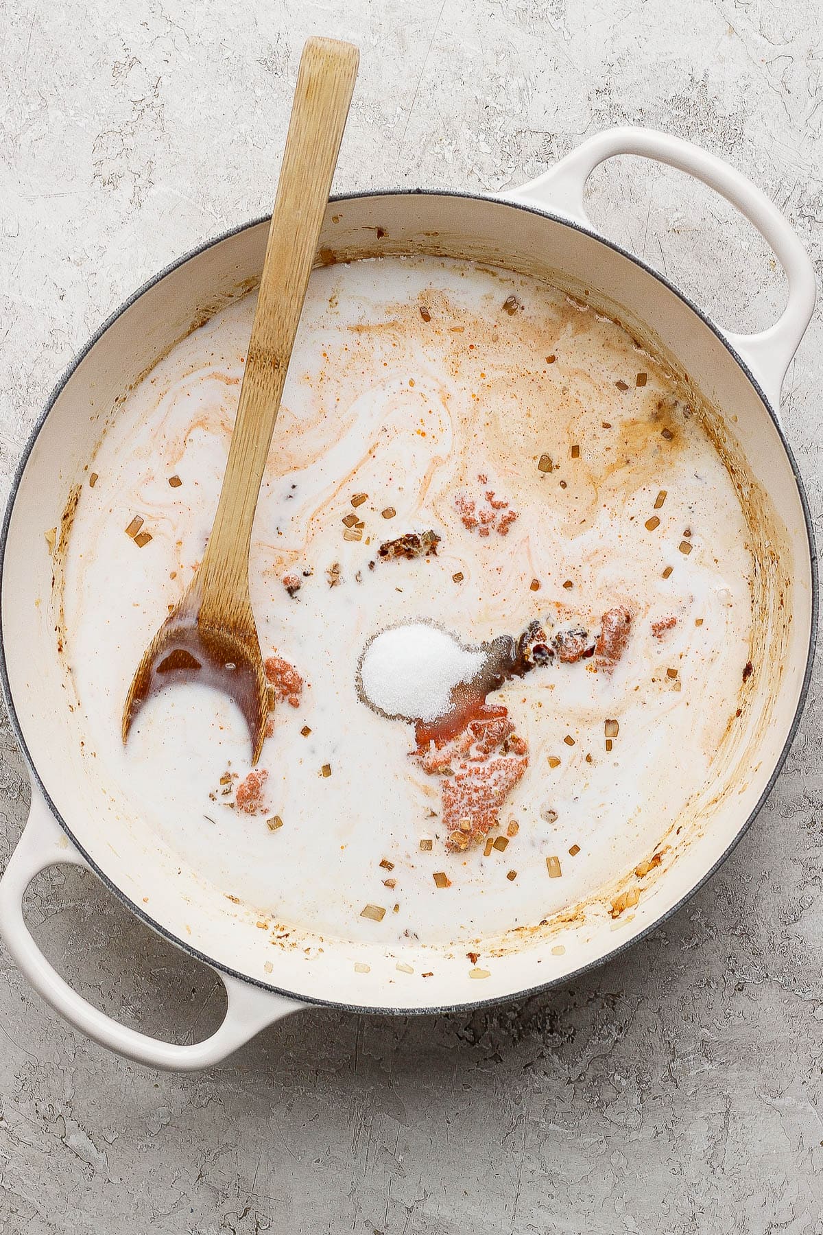 Sweet curry sauce ingredients in a braising pan with a wooden spoon sticking out the side.