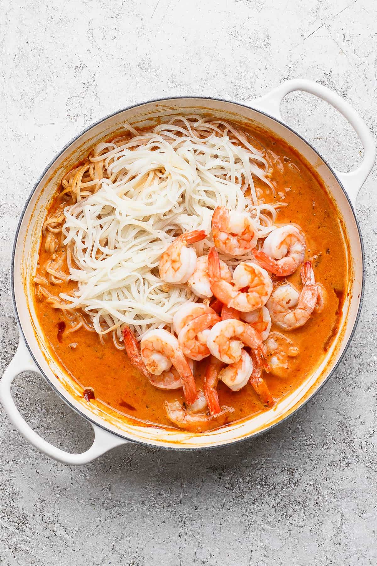 Shrimp and rice noodles added to a braising pan of simmering sweet curry sauce.
