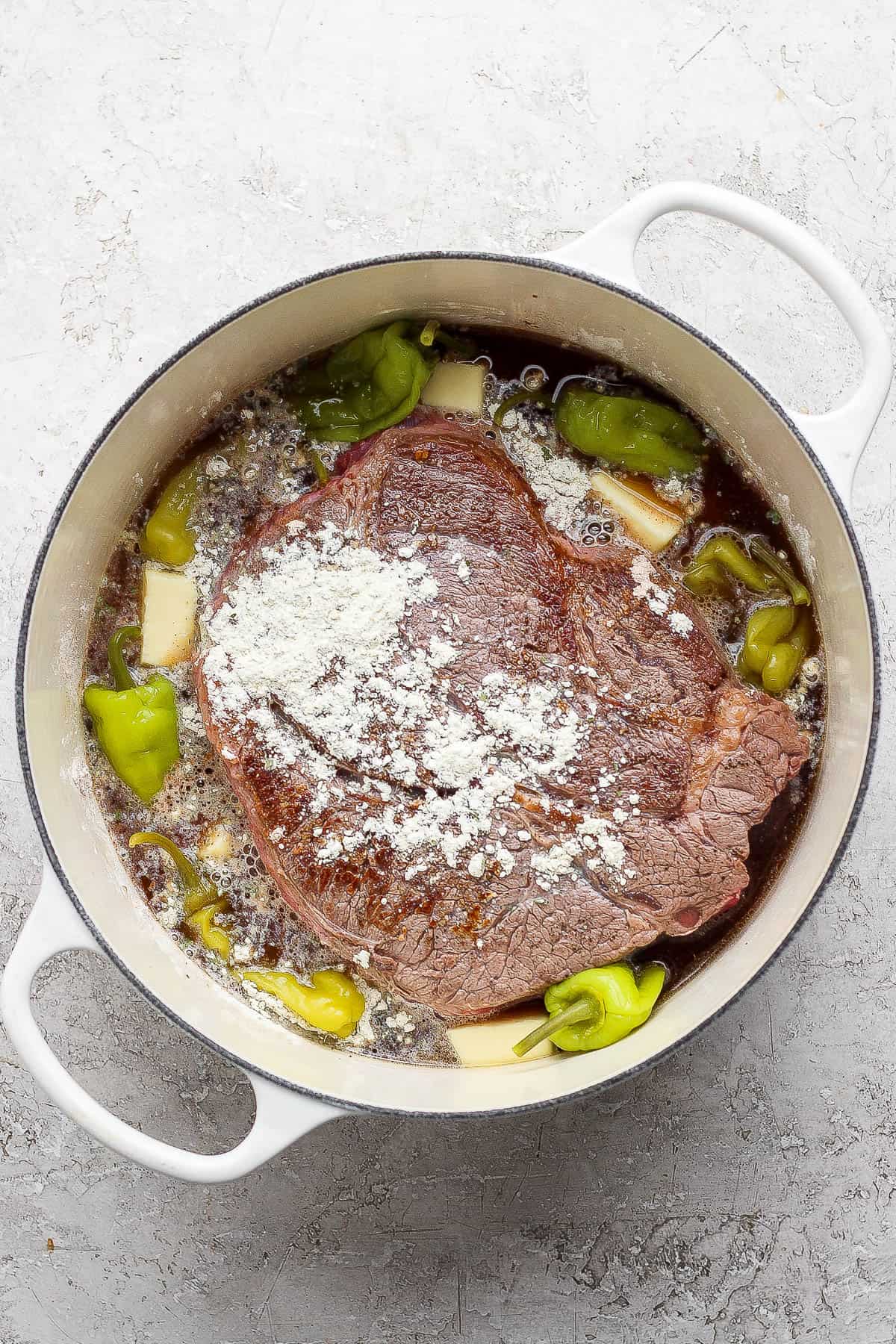 Beef broth, gravy packet, ranch seasoning packet, butter, and pepperocini peppers in the dutch oven to make dutch oven mississippi pot roast.