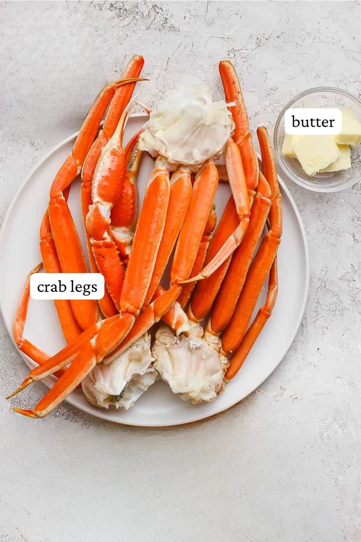 Snow crab legs on a white plate next to a small dish of butter with labels.