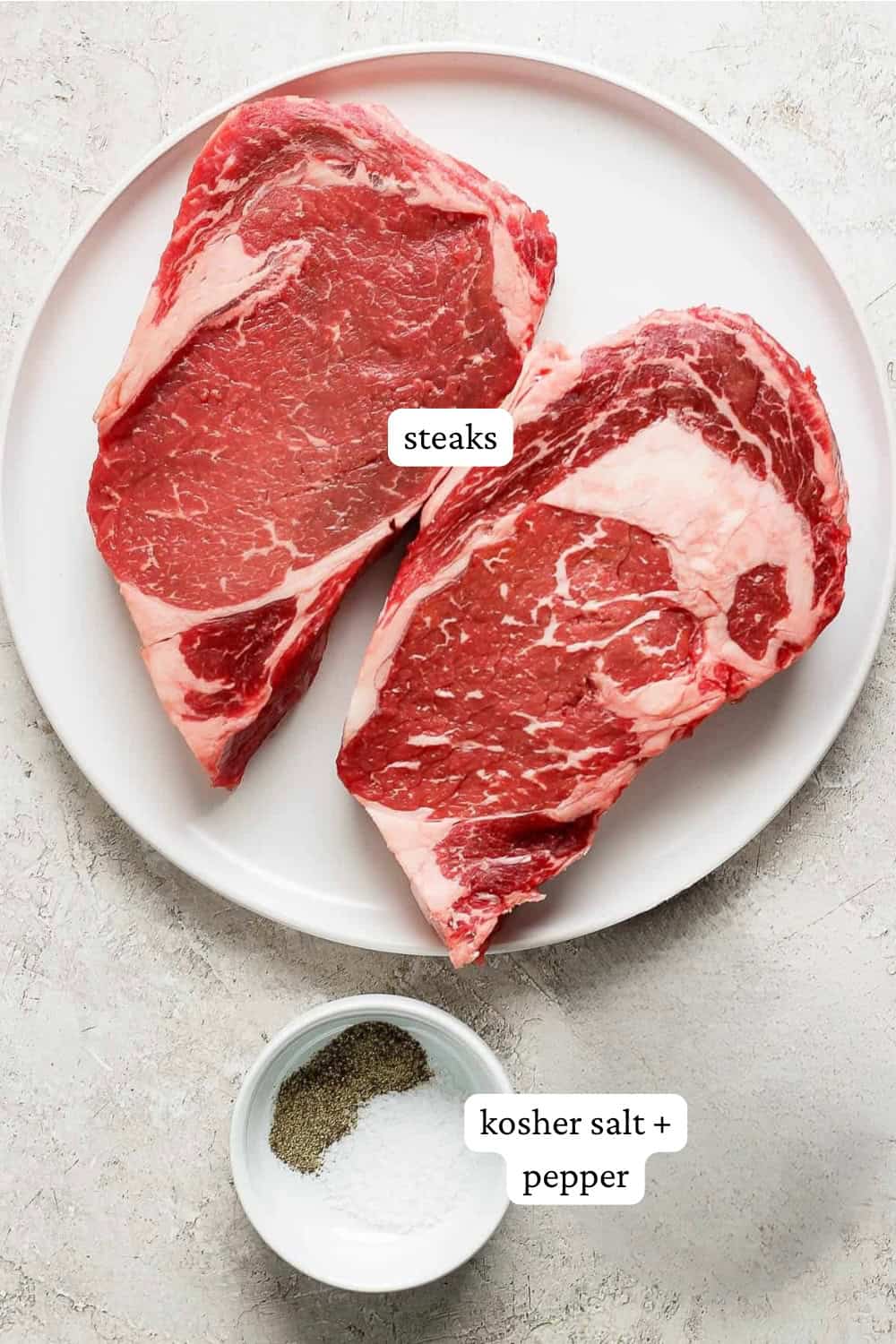 A plate of steaks next to a small dish of salt and pepper with labels.