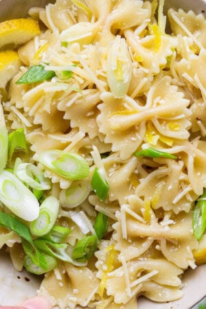 Lemon pasta salad in a bowl with slices of lemon and green onions.
