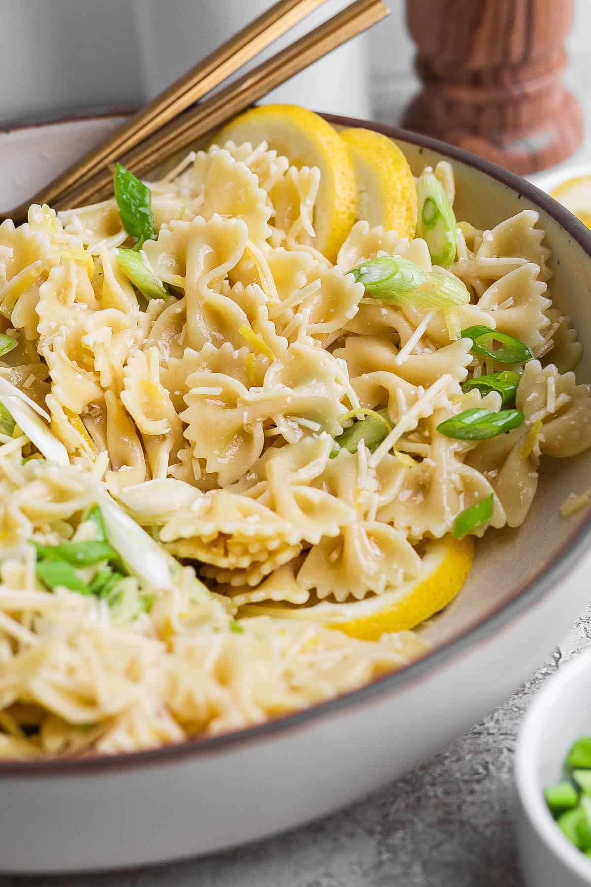 A fully mixed bowl of lemon pasta salad with two gold spoons sticking out the side.