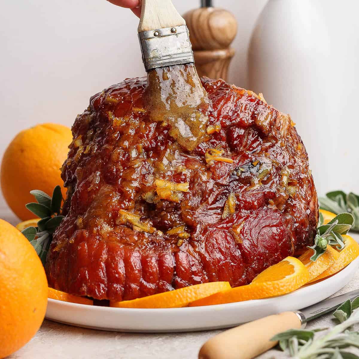 A fully cooked orange glazed ham on a platter being brushed with more glaze.