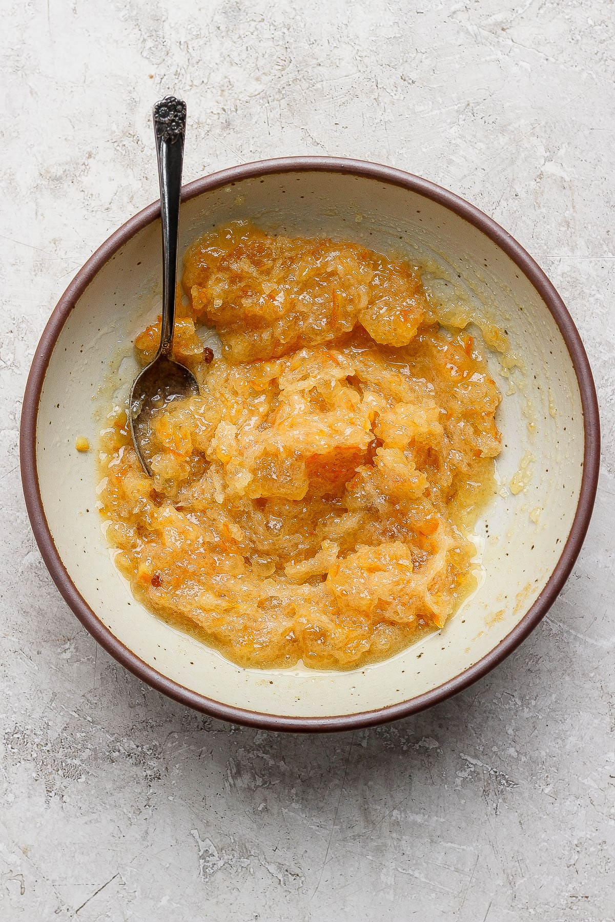Orange glaze for an orange glazed ham mixed in a bowl with a spoon sticking out the side.